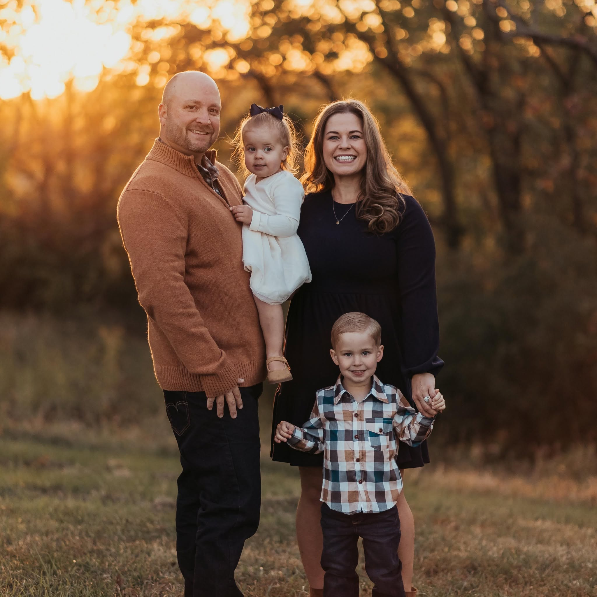 Family of four standing together outdoors at sunset.
