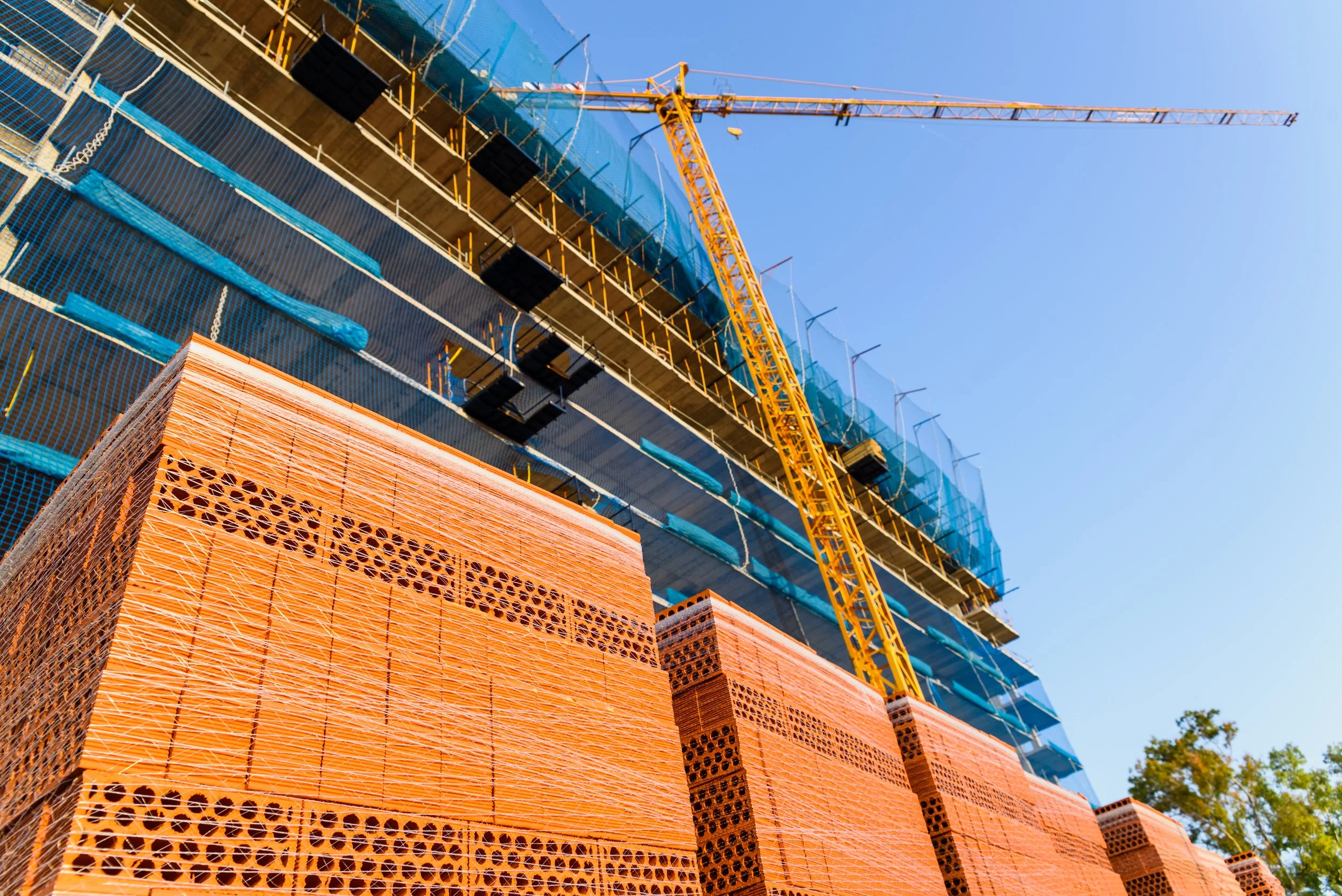 Active commercial construction site with tower crane, building structure, scaffolding, and construction materials.