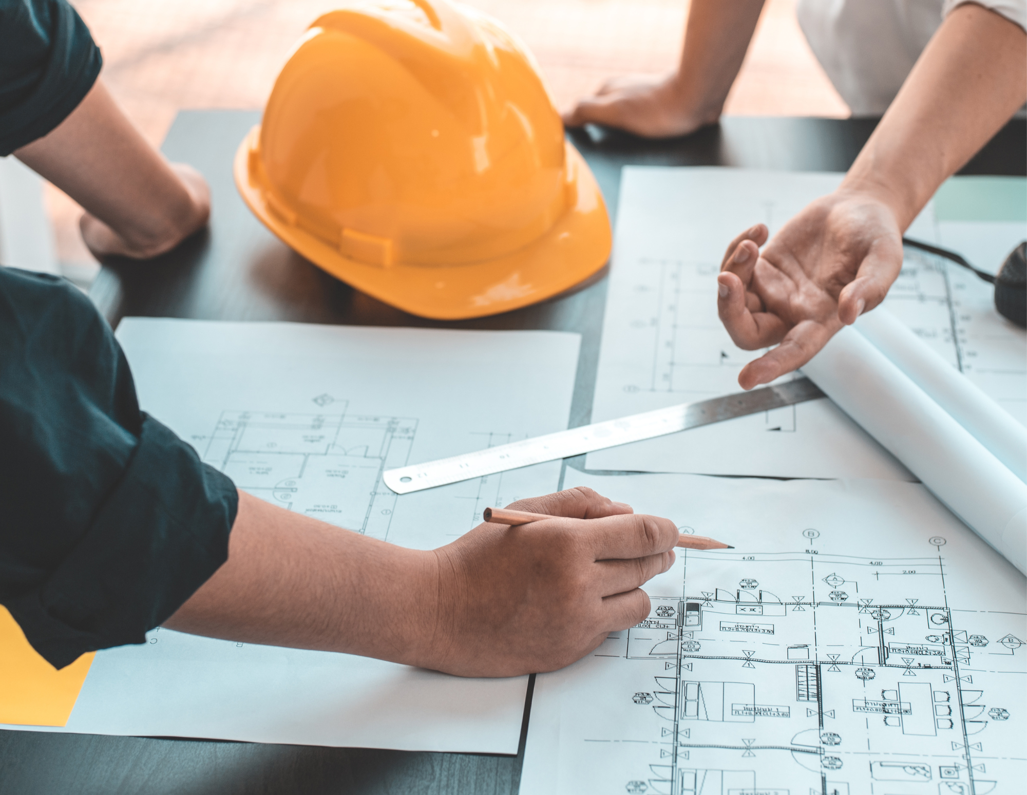 People discussing architectural blueprints in an office, with a yellow construction helmet on the table.