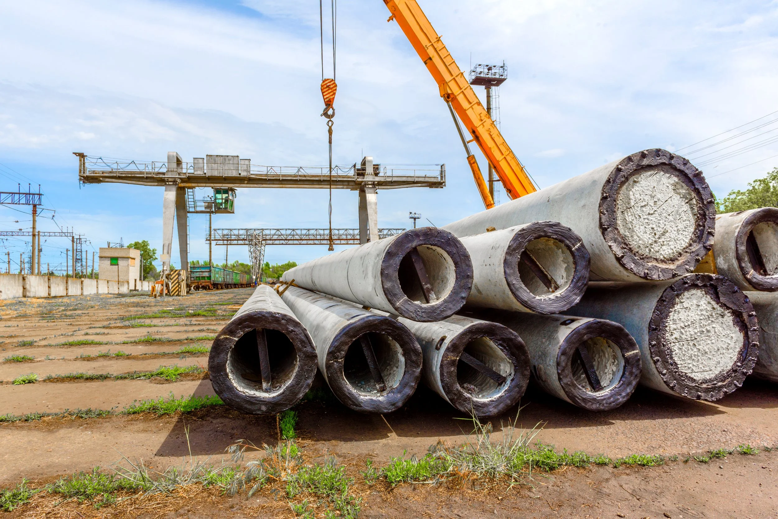 Concrete pipes staged at an active construction site while a crane performs installation work.