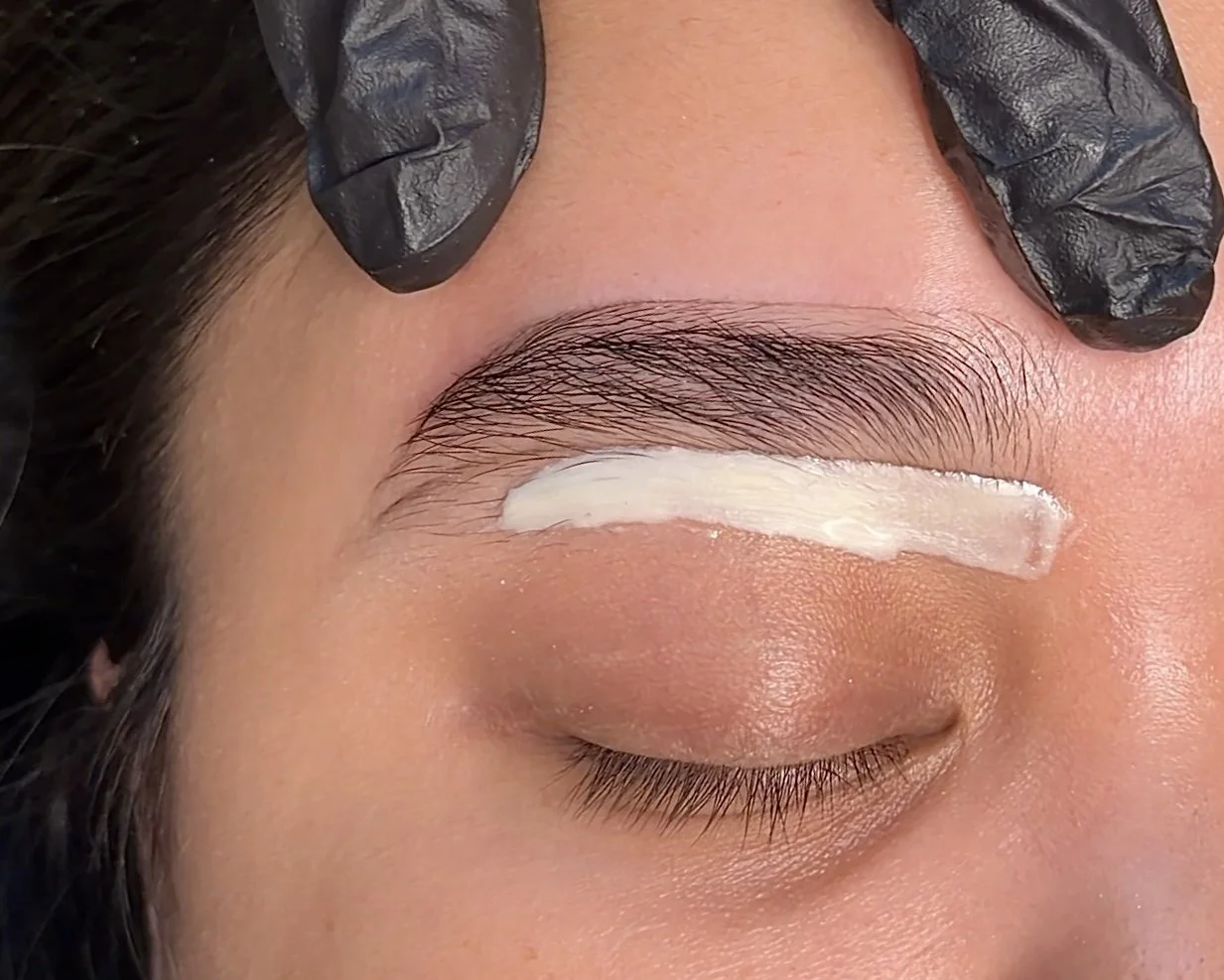 A person with their eyes closed and a layer of white cream or lotion applied to their eyelid, with a gloved hand nearby.