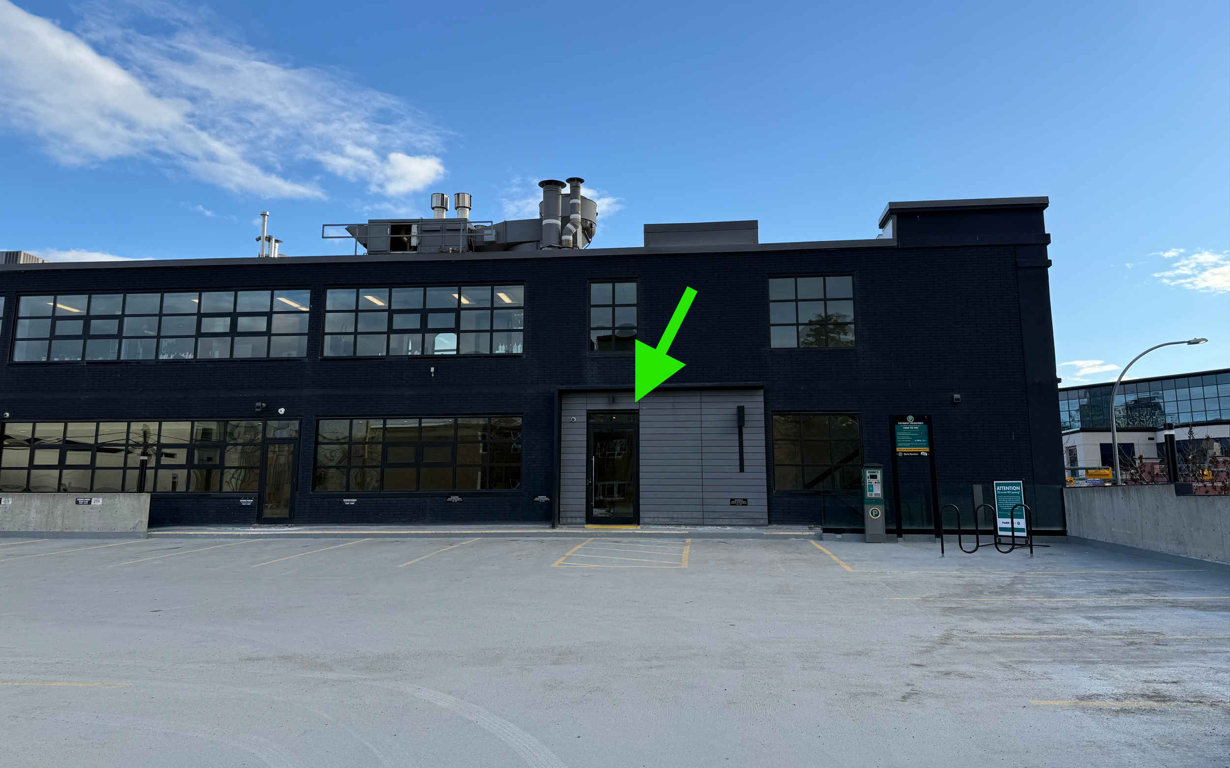 Modern black building with large windows and a loading dock with a green arrow pointing to a door.