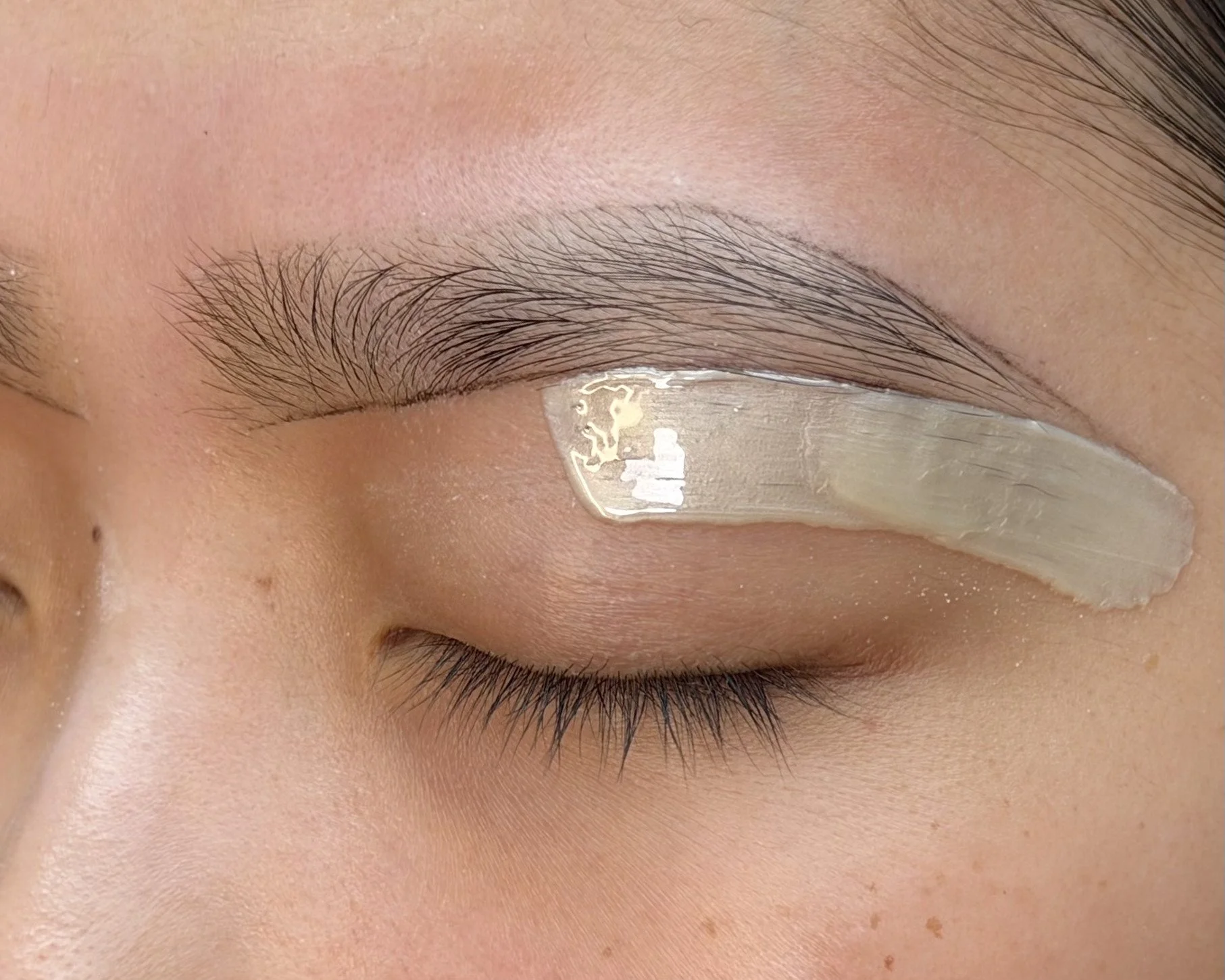 Close-up of a person's closed eye with natural eyelashes, eyebrow, and skin details visible, and an adhesive eye mask applied beneath the eye.