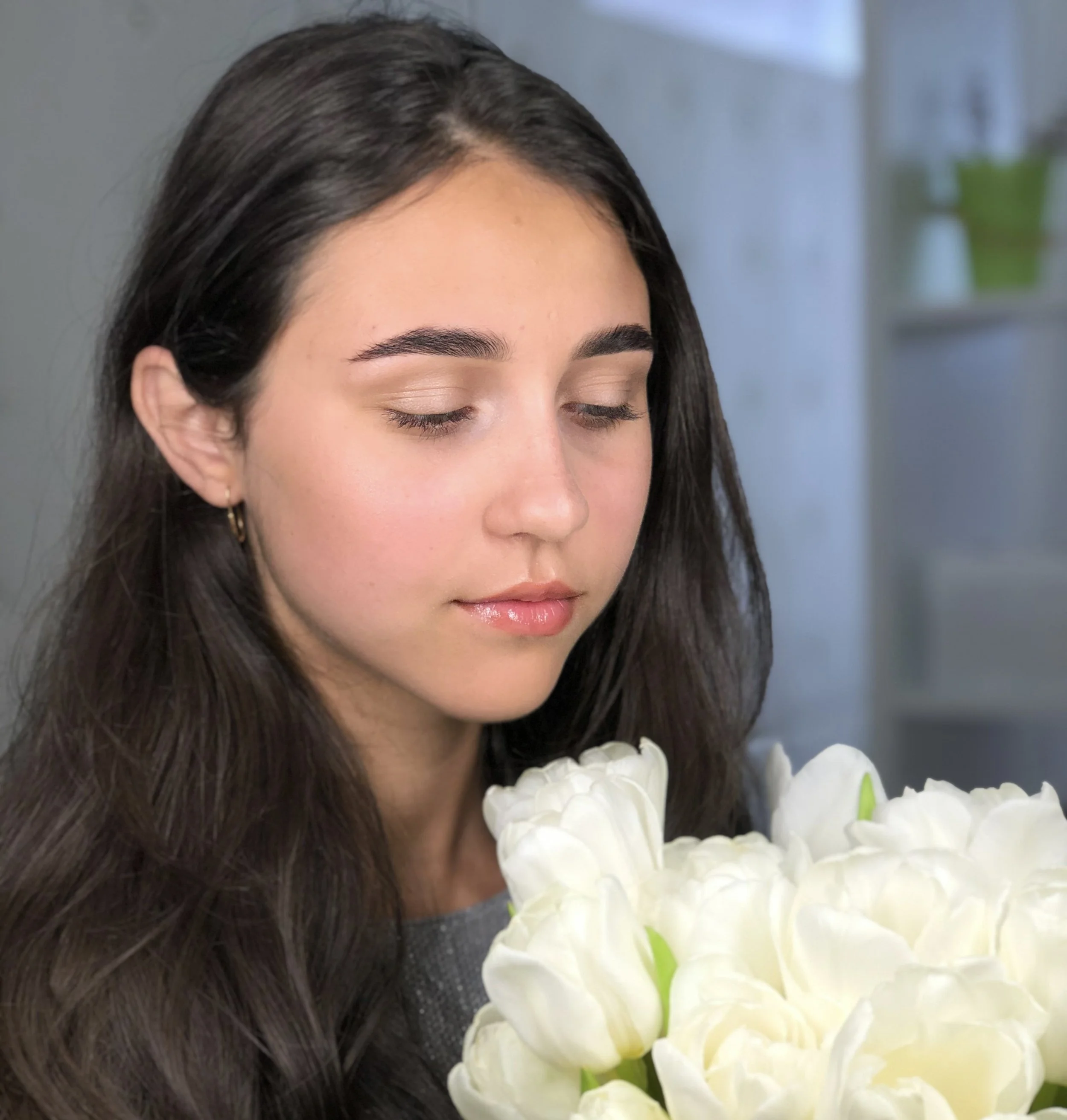 A woman with long dark hair and closed eyes smelling white flowers.