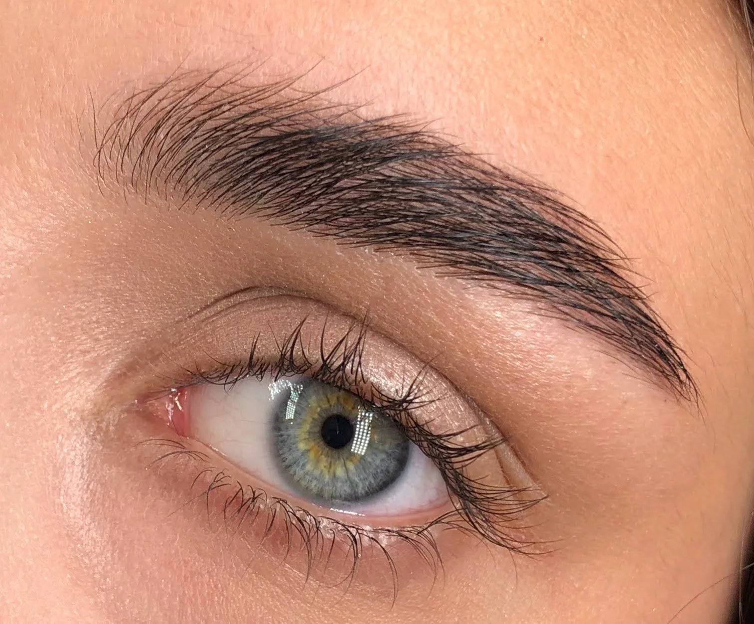 Close-up of a human eye with green and hazel iris, slightly parted eyelid, and well-groomed eyebrow.