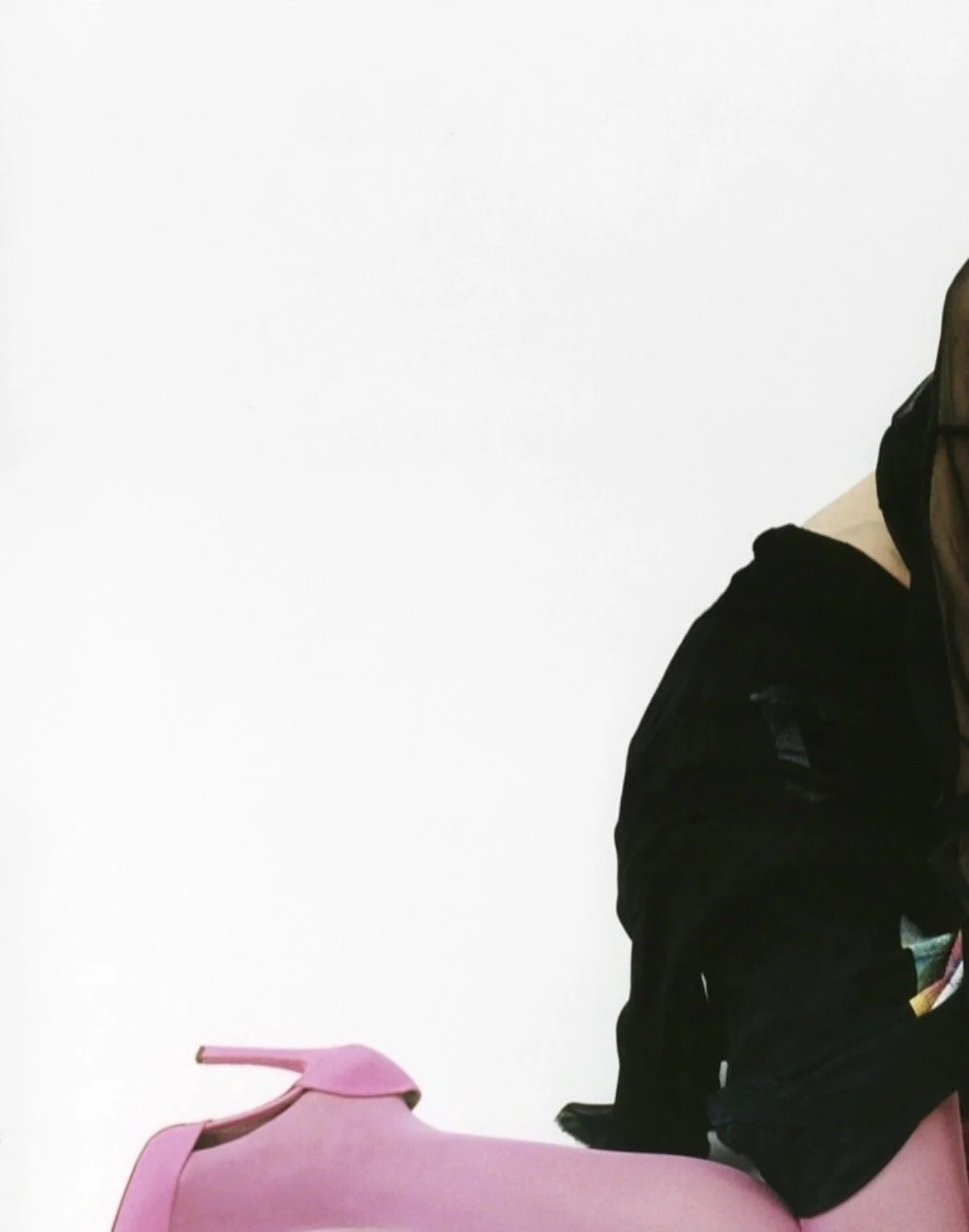 A person dressed in black sitting on a pink chair with a large white wall in the background.