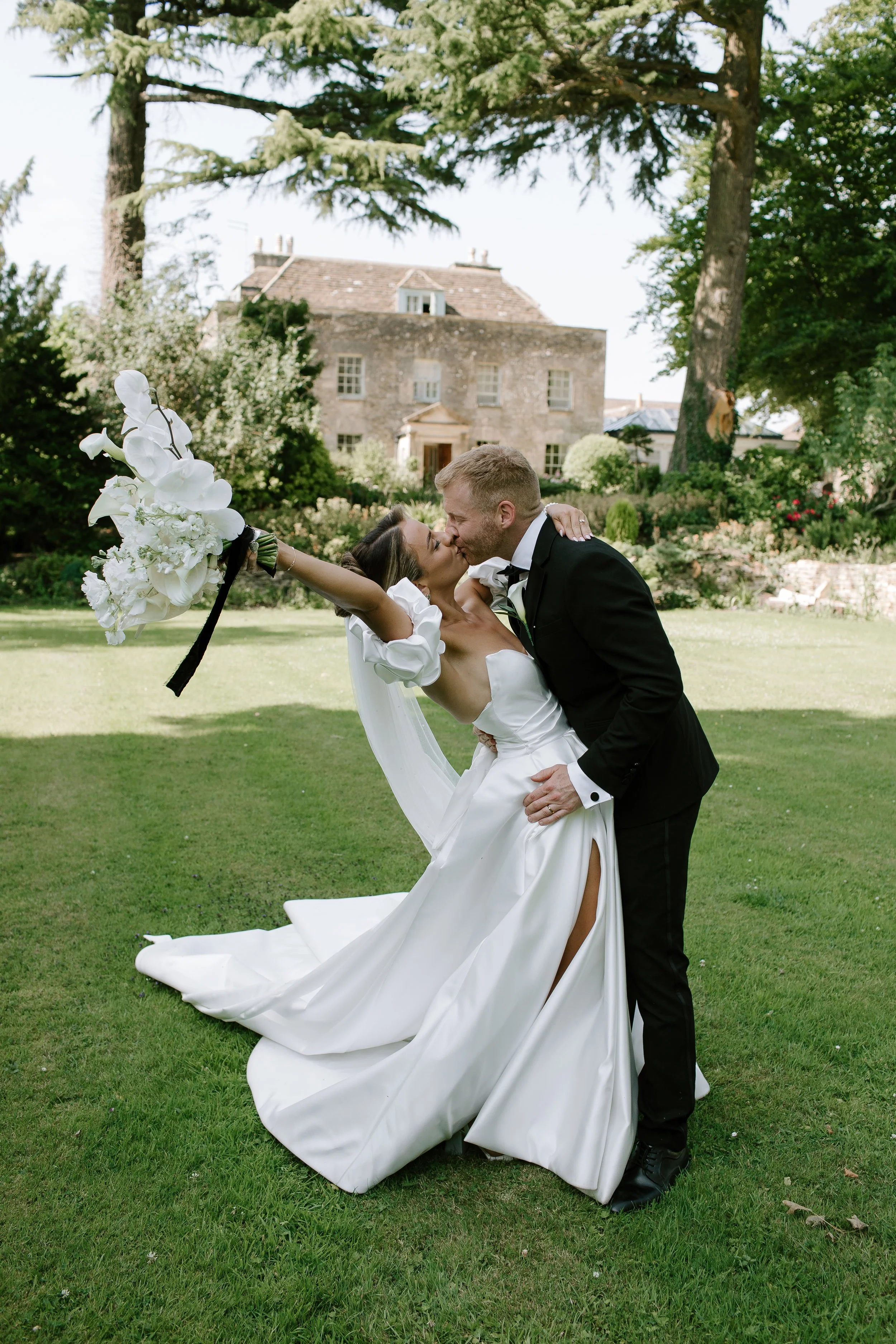 Bride and groom sharing a kiss while celebrating in the gardens of a Somerset country house wedding venue during relaxed wedding portraits.