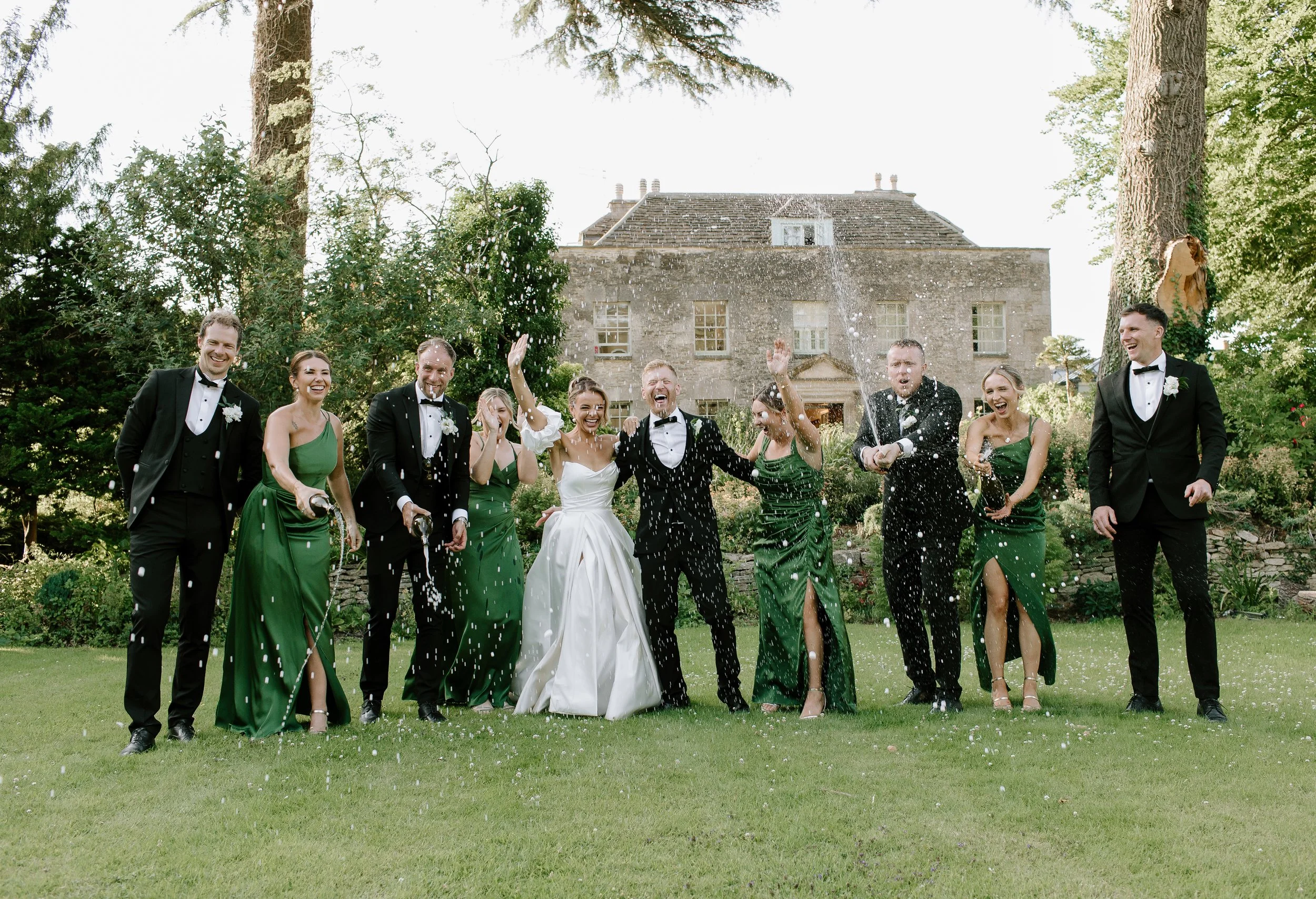 oyful wedding party celebrating with champagne outside a country house wedding venue in Somerset.