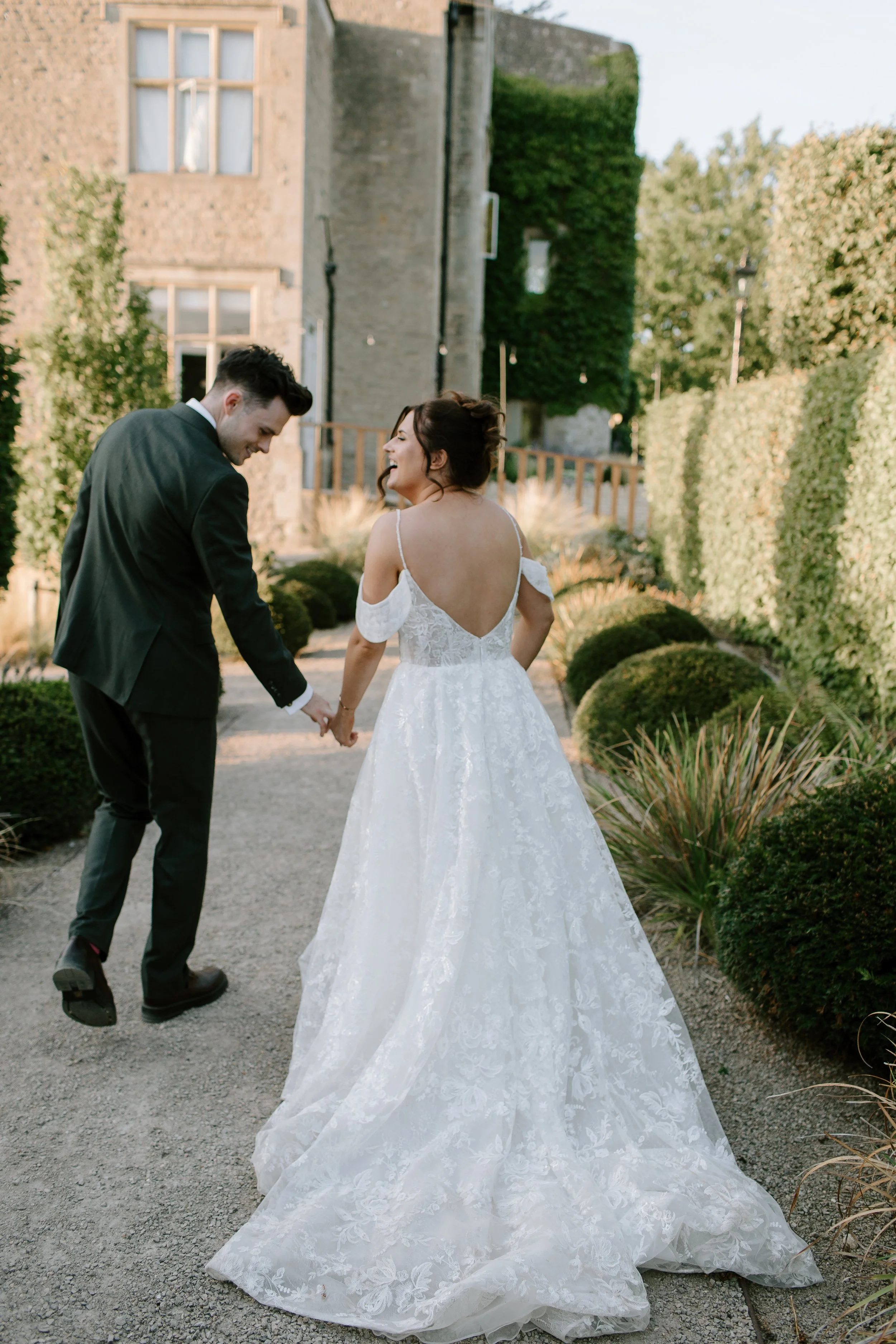 Bride and groom walking hand in hand through the gardens of a Somerset country house wedding venue during relaxed wedding portraits.