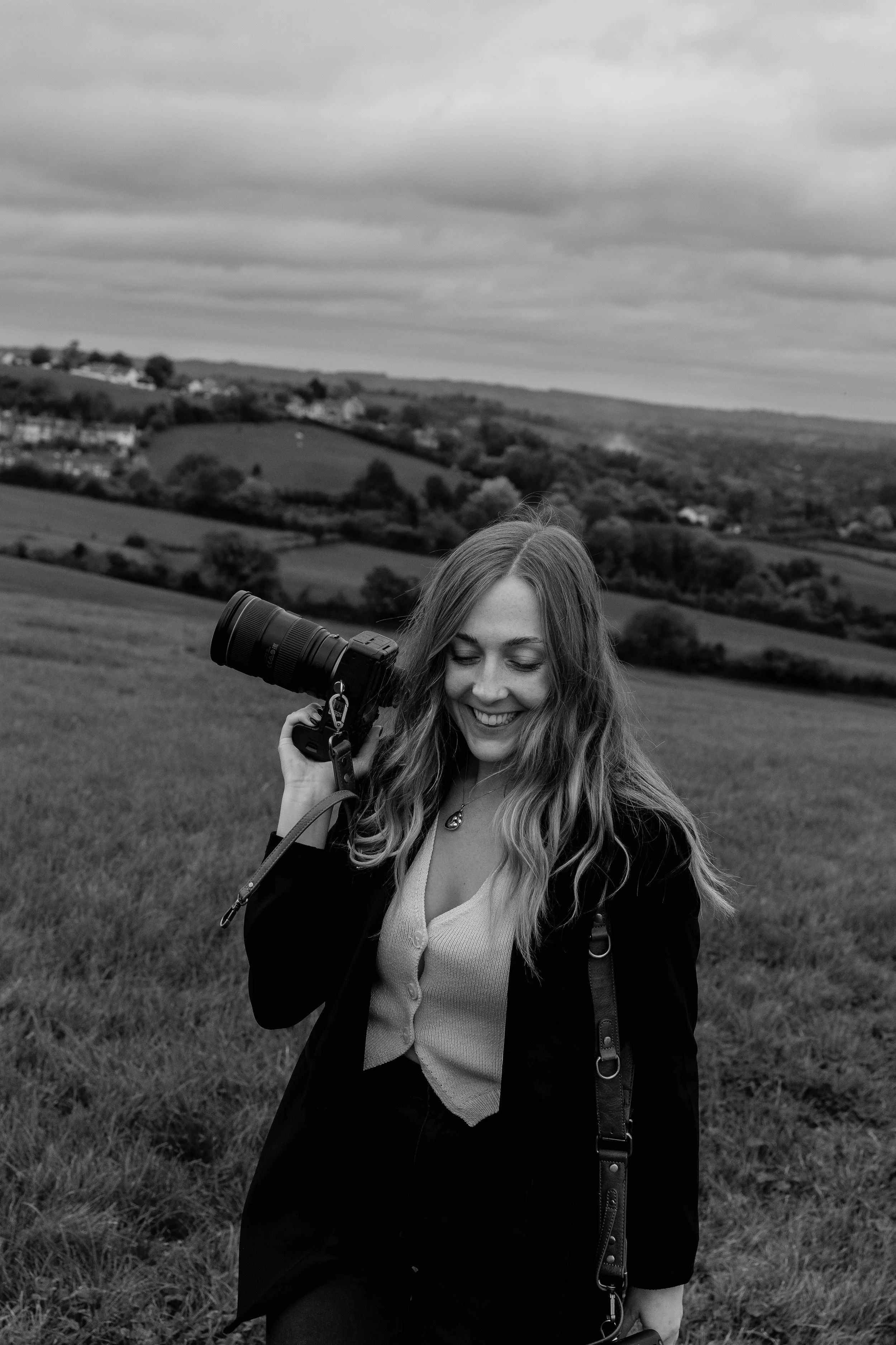 Somerset wedding photographer holding a camera and smiling while walking through countryside during a personal branding photoshoot.
