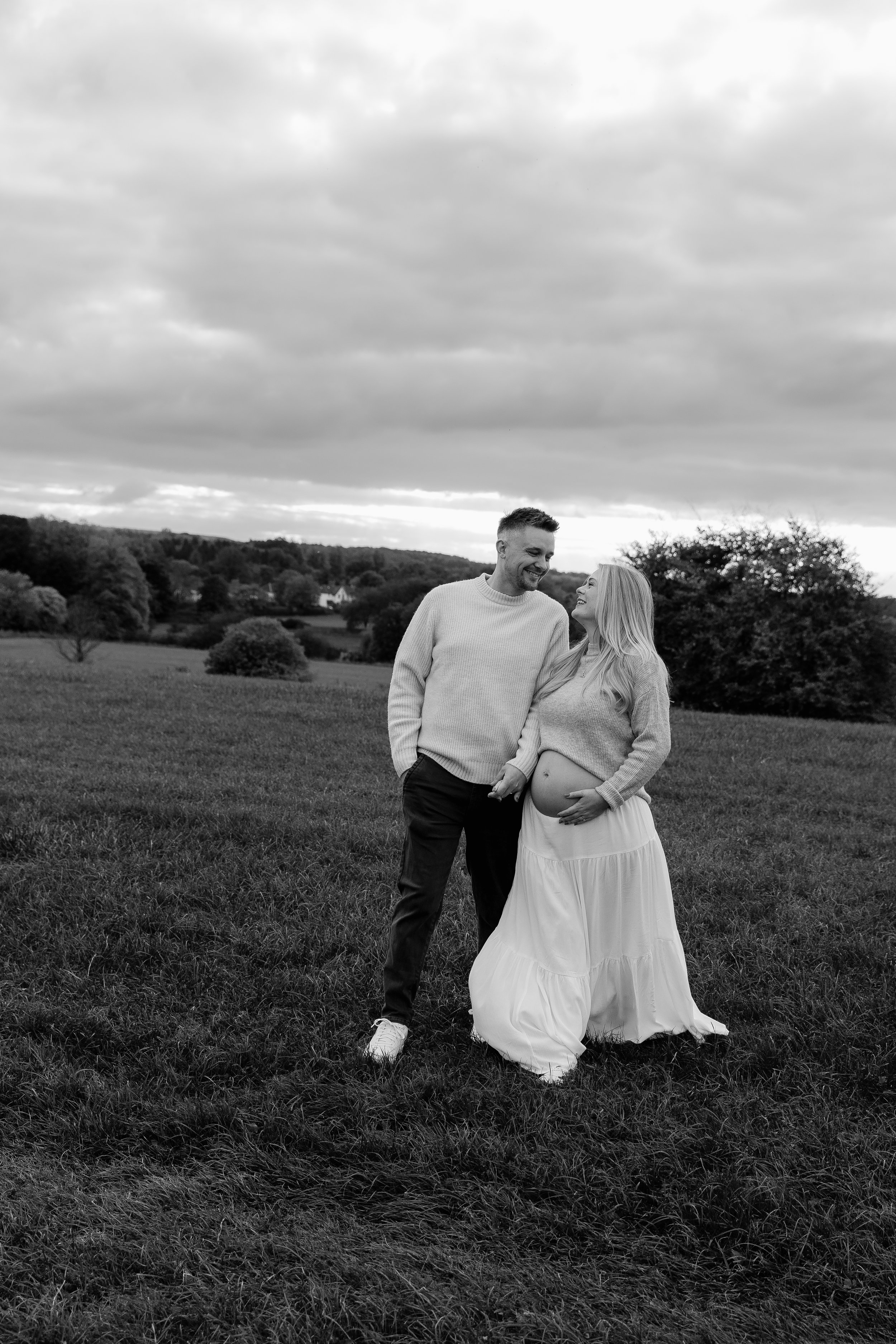 Relaxed black and white maternity photography in Somerset of an expectant couple standing together in a rural field.