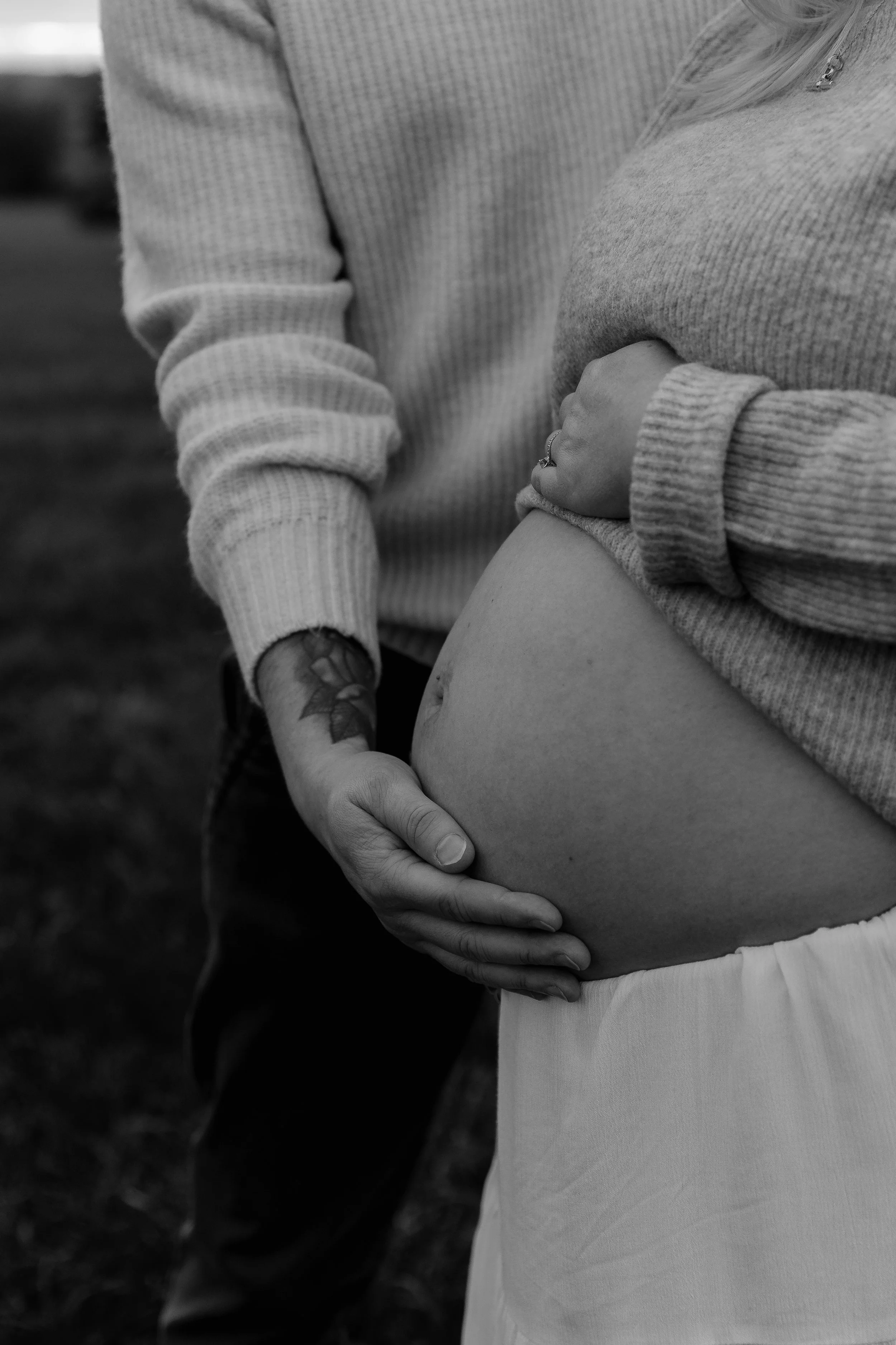 Black and white maternity photoshoot in Mells, Somerset capturing an expectant couple’s hands resting on a pregnant belly outdoors