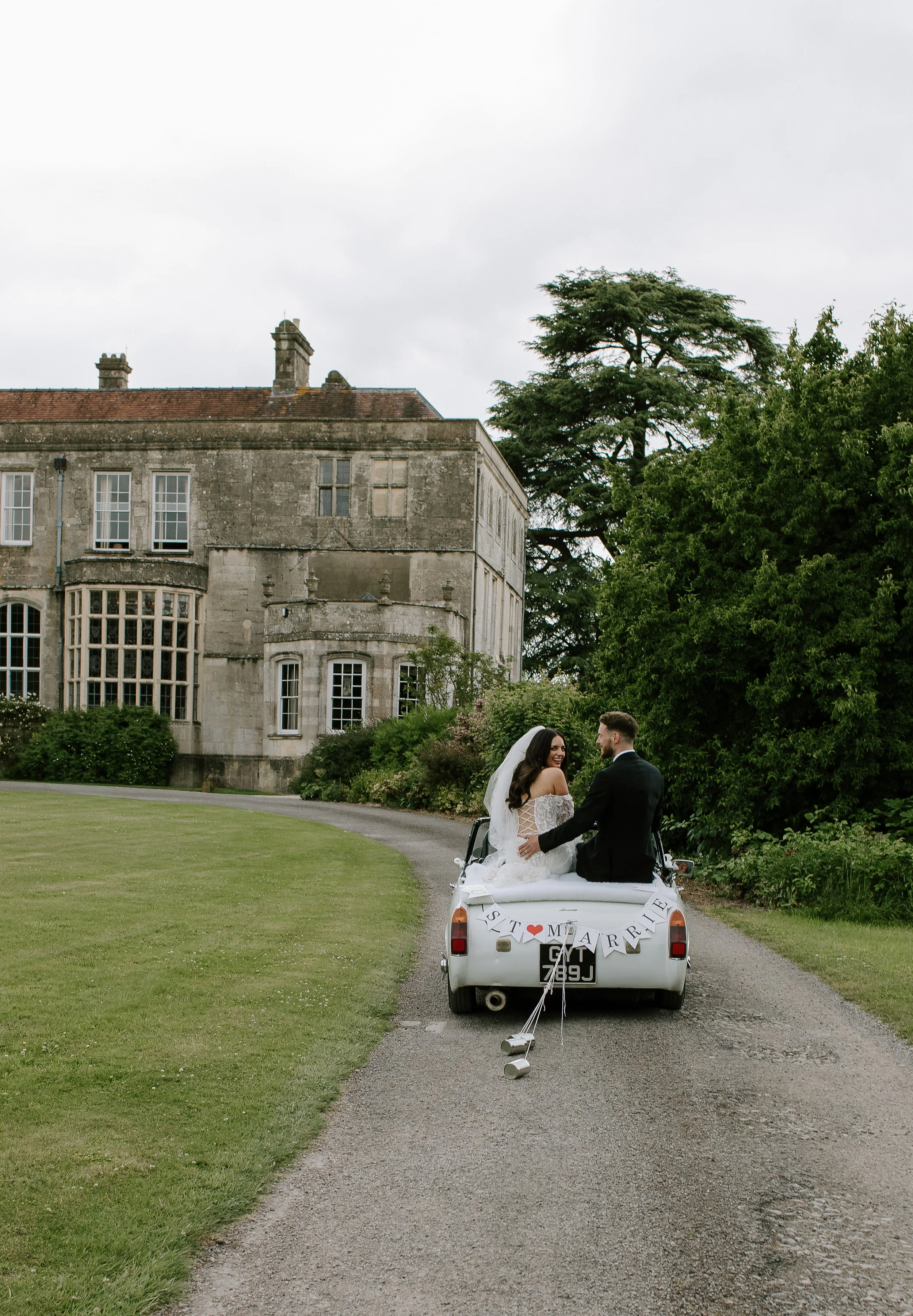 Bride and groom sitting in the back of a wedding car outside a country house during a Somerset wedding.