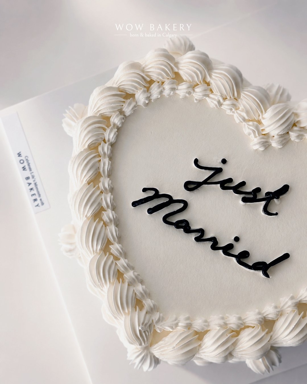 White vintage heart-shaped wedding cake with piped cream border and “Just Married” lettering