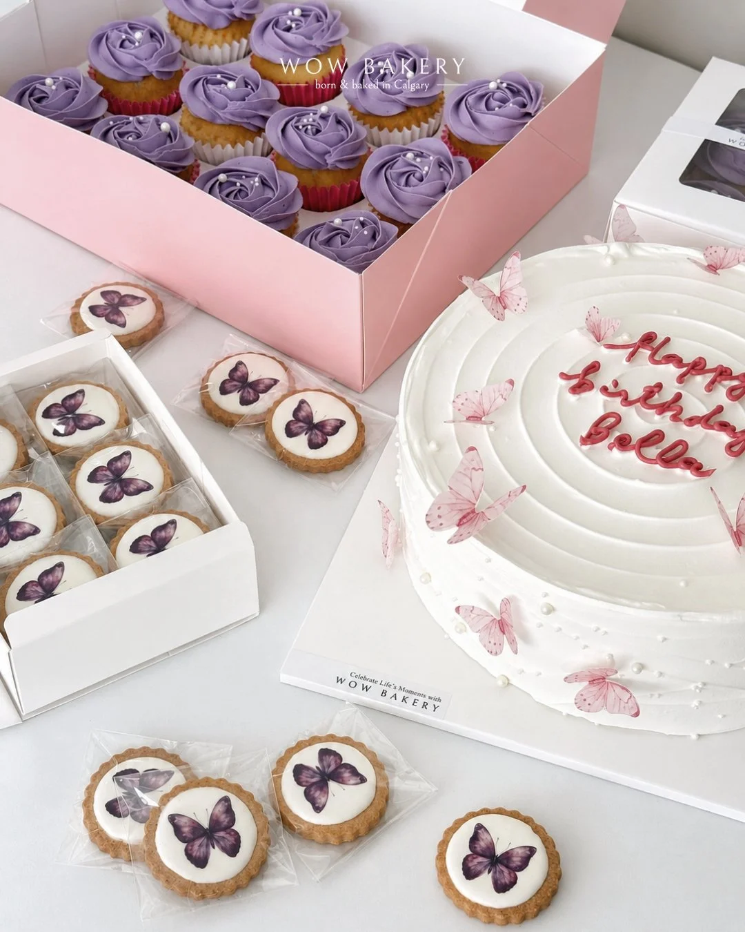 A celebration dessert spread with purple cupcakes, butterfly cookies, and a white birthday cake decorated with pink butterflies.