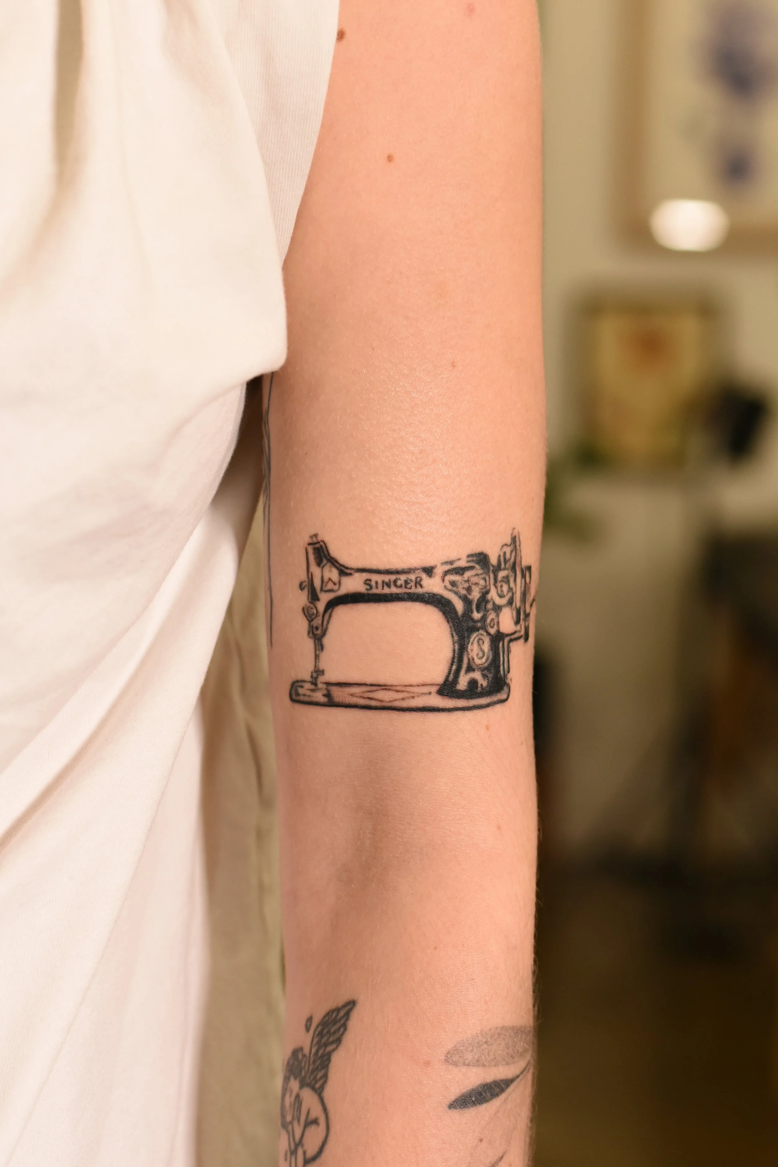 Tattoo of a vintage Singer sewing machine on a person's forearm.