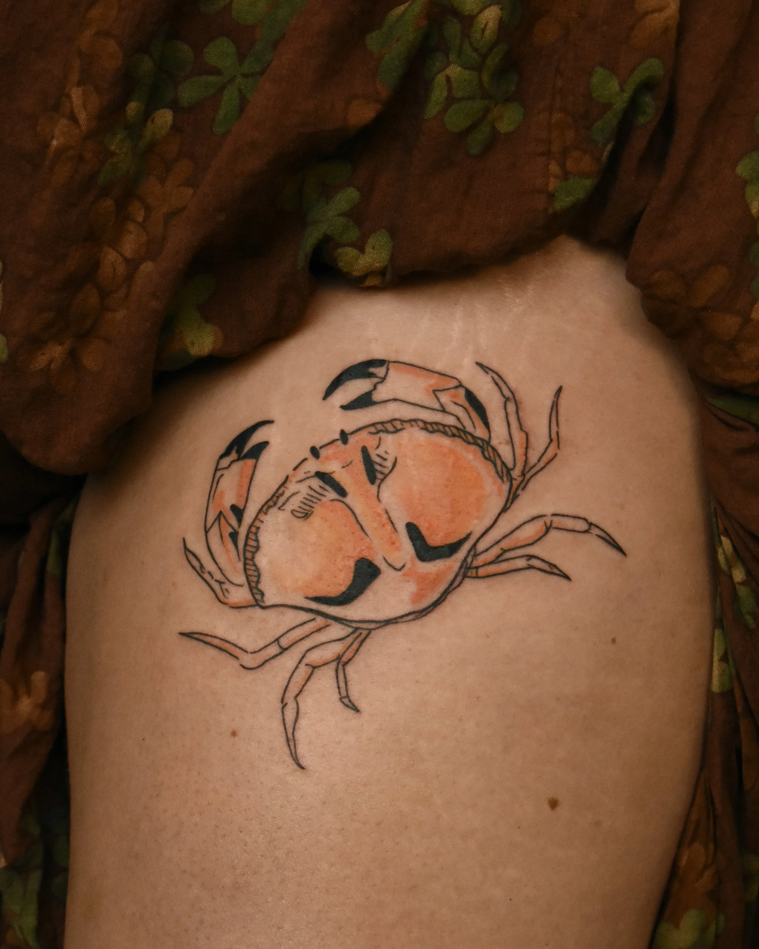 Tattoo of a crab with orange and black detail on someone's arm.