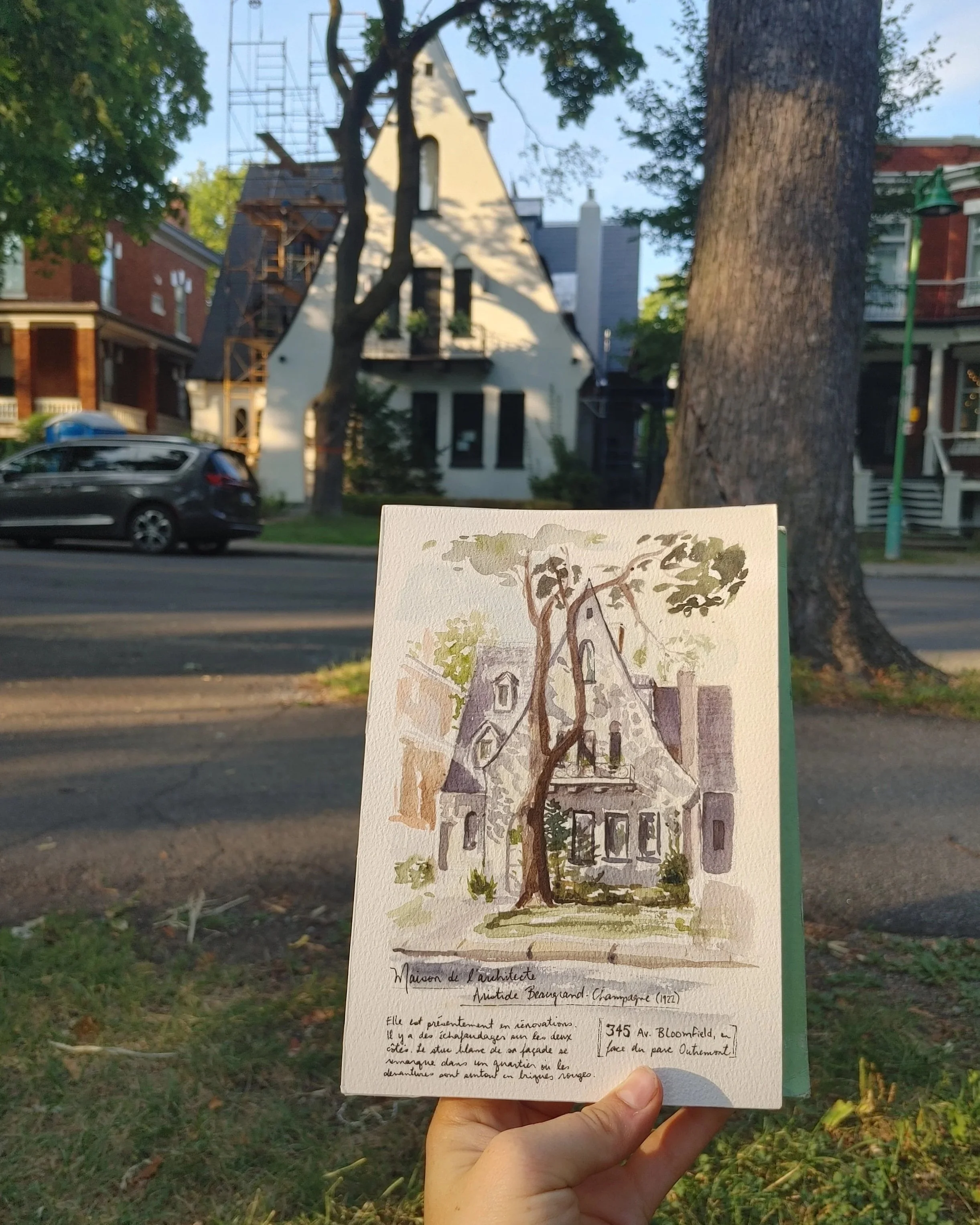 Watercolor urban sketch of an old house in Outremont, Montréal,  held by a hand in front of the house in parc Outremont, Montreal..
