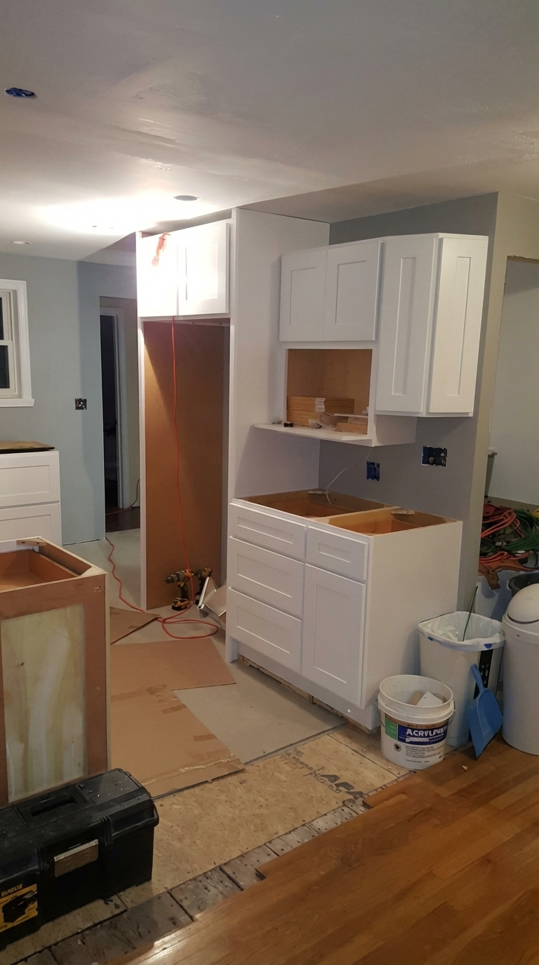 Kitchen renovation in progress with white cabinets, unfinished countertops, construction tools, and supplies.