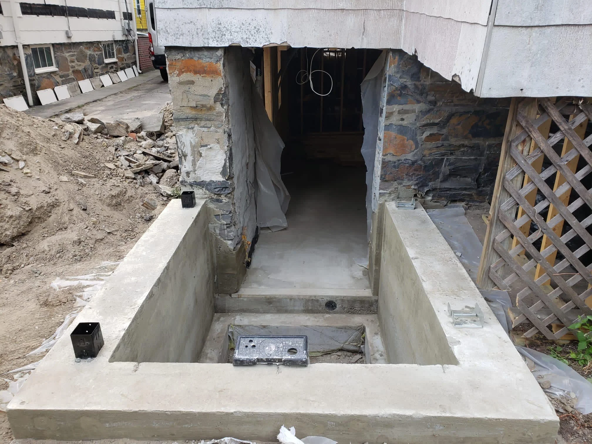 Concrete steps leading to an underground area under construction, with metal bolts in the steps and exposed stone and wood framing around the entrance.