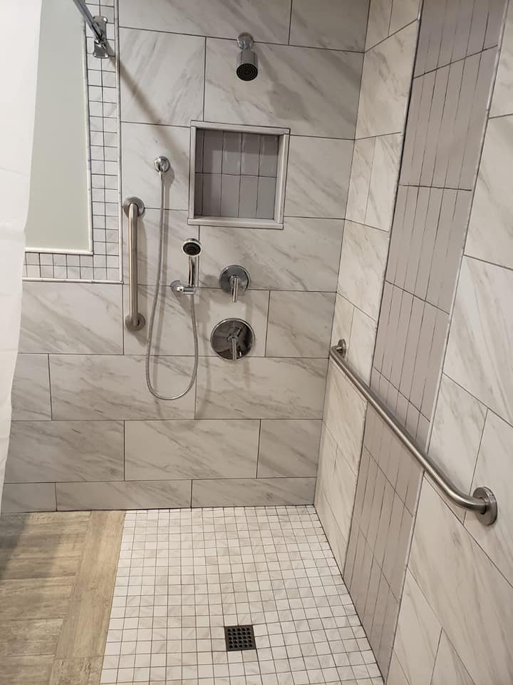 Accessible shower with wall-mounted shower head, handheld shower, built-in niche, grab bars, and tiled walls and floor.
