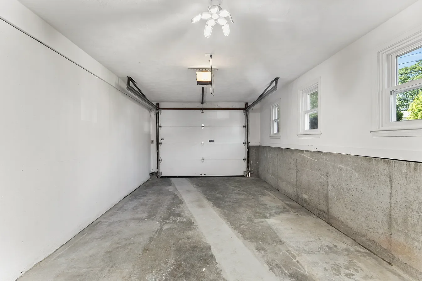 Empty residential garage with concrete floor, white walls, three windows, and a closed garage door