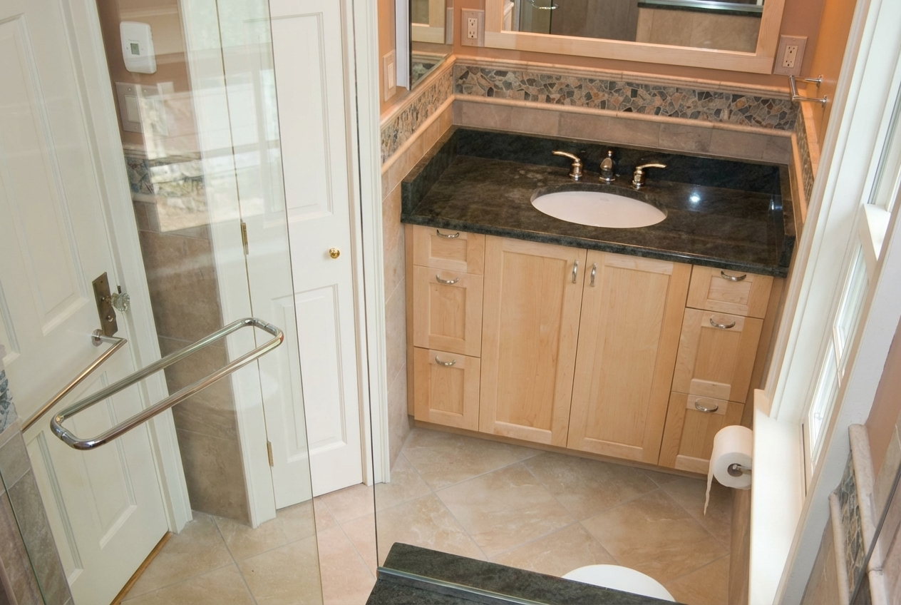 A bathroom with a black marble countertop, wooden cabinets, a mirror, a toilet paper roll, and a glass shower door.