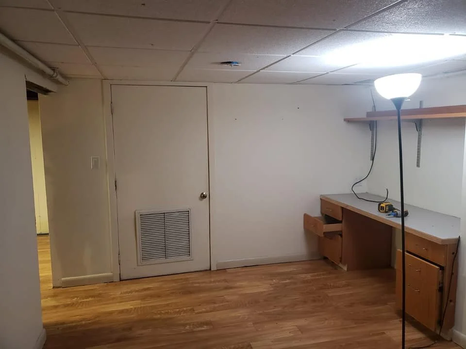 Empty room with a white wall, wooden furniture, and a standing lamp.