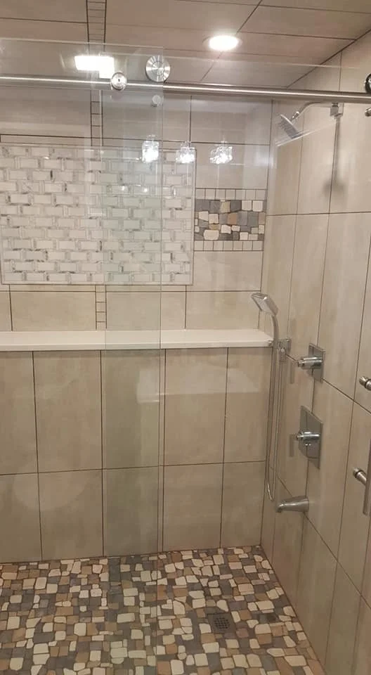 A modern shower with beige tiles, a built-in bench, a glass door, a rainfall showerhead, and multiple body spray jets.