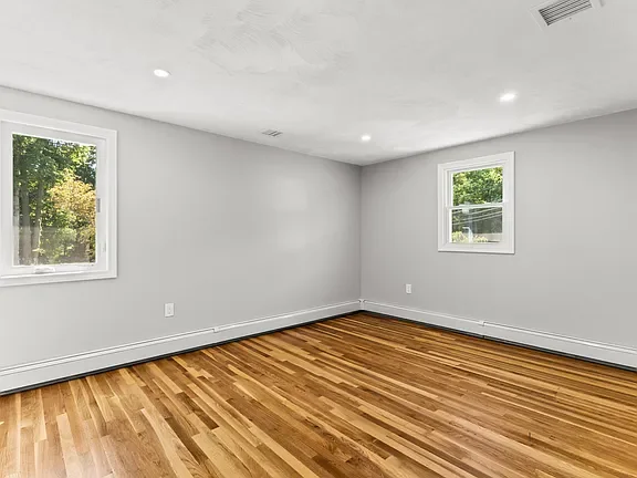 Empty room with hardwood floors, white walls, two windows, and ceiling lights.