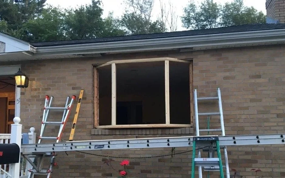 Construction project to build a framed window opening on a brick house, with ladders leaning against the wall and a level placed on a scaffold.