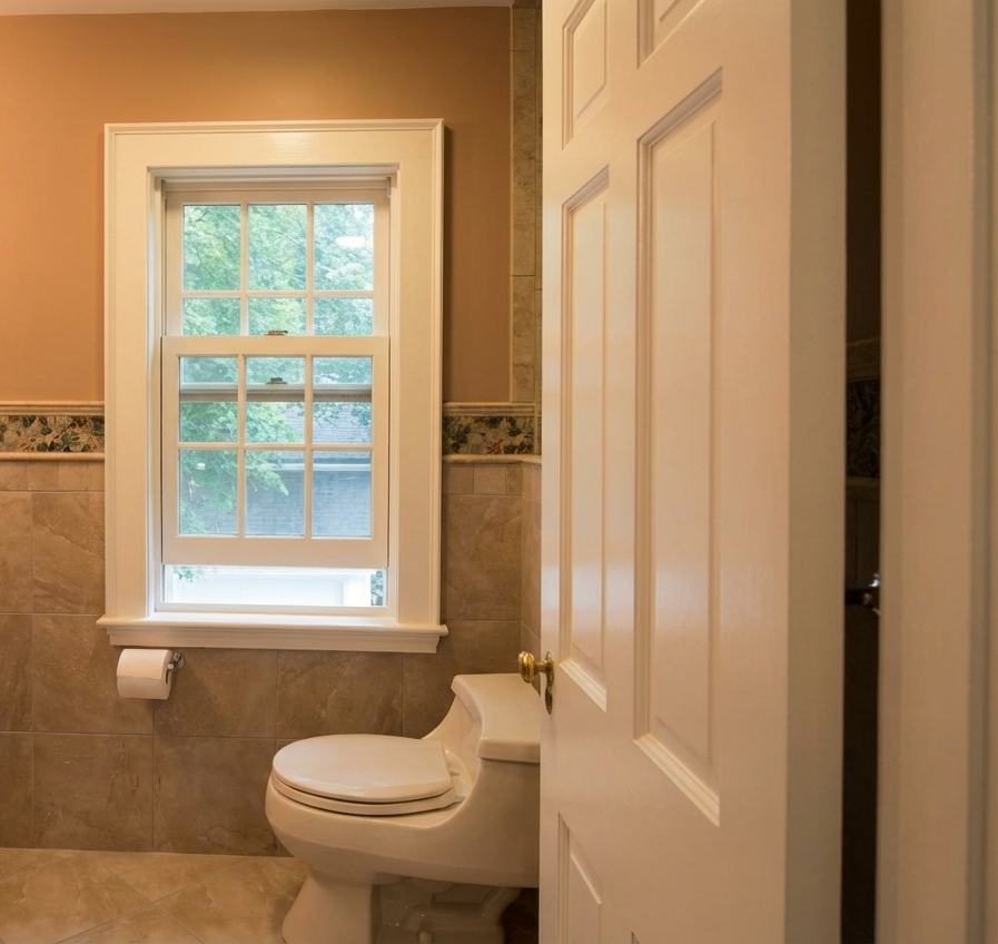 A bathroom with a white toilet, a window with multiple panes, and a partially open door.