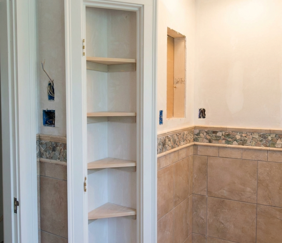 Bathroom with unfinished electrical wiring and a built-in corner shelf unit.