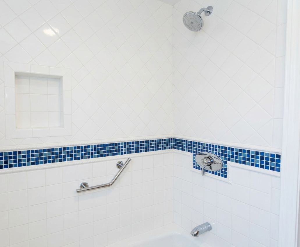 A shower with white tiled walls, a built-in niche, a blue mosaic tile border, a silver handheld showerhead, temperature control, and a grab bar.