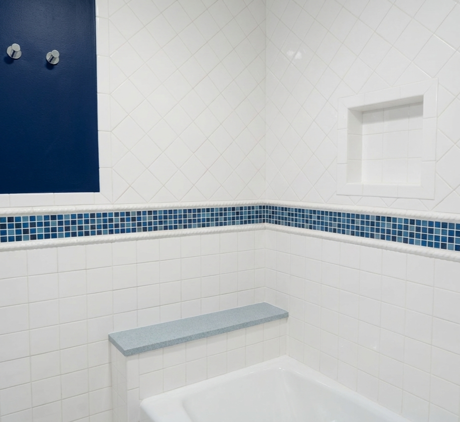 Bathroom with white tile walls, a blue accent strip, a built-in niche, and a small granite ledge above a bathtub.