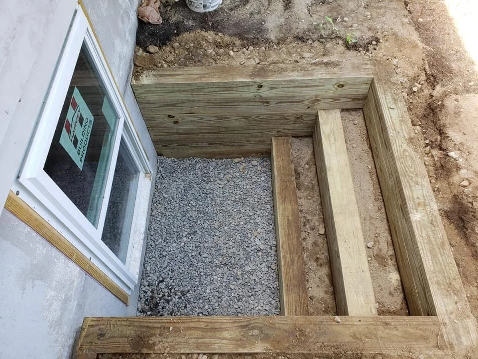 Close-up of a building foundation with wooden framing and gravel ground near a window.