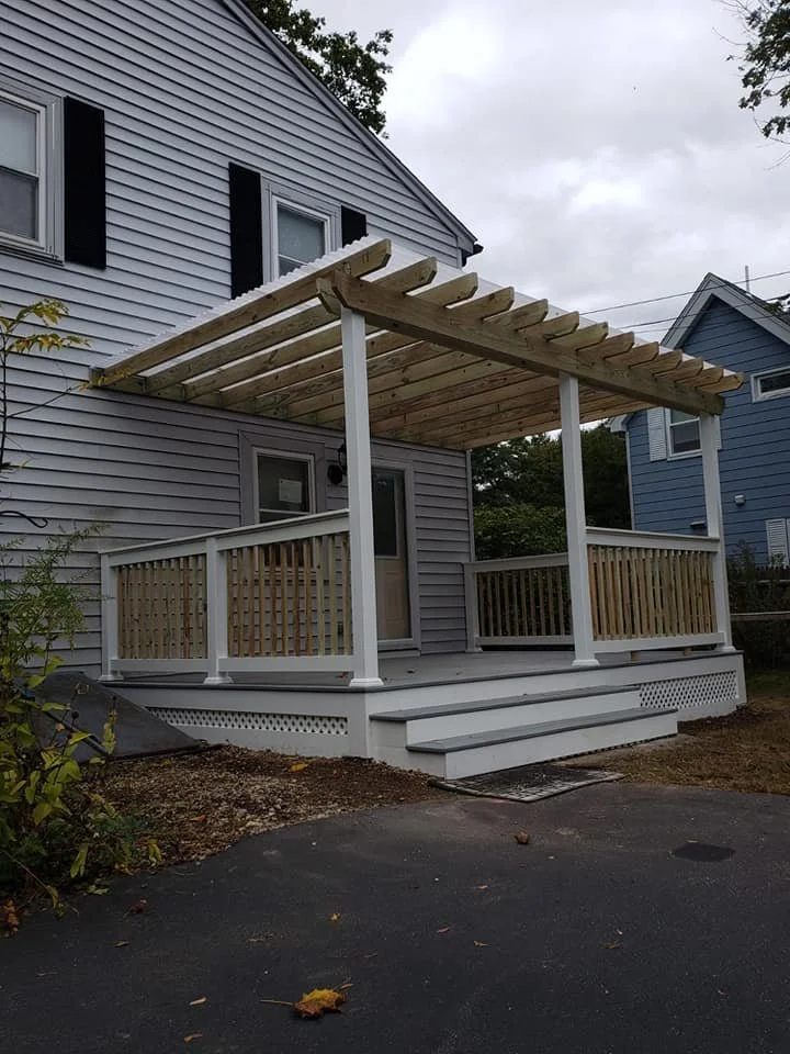 A newly built front porch with a pergola on a blue house.