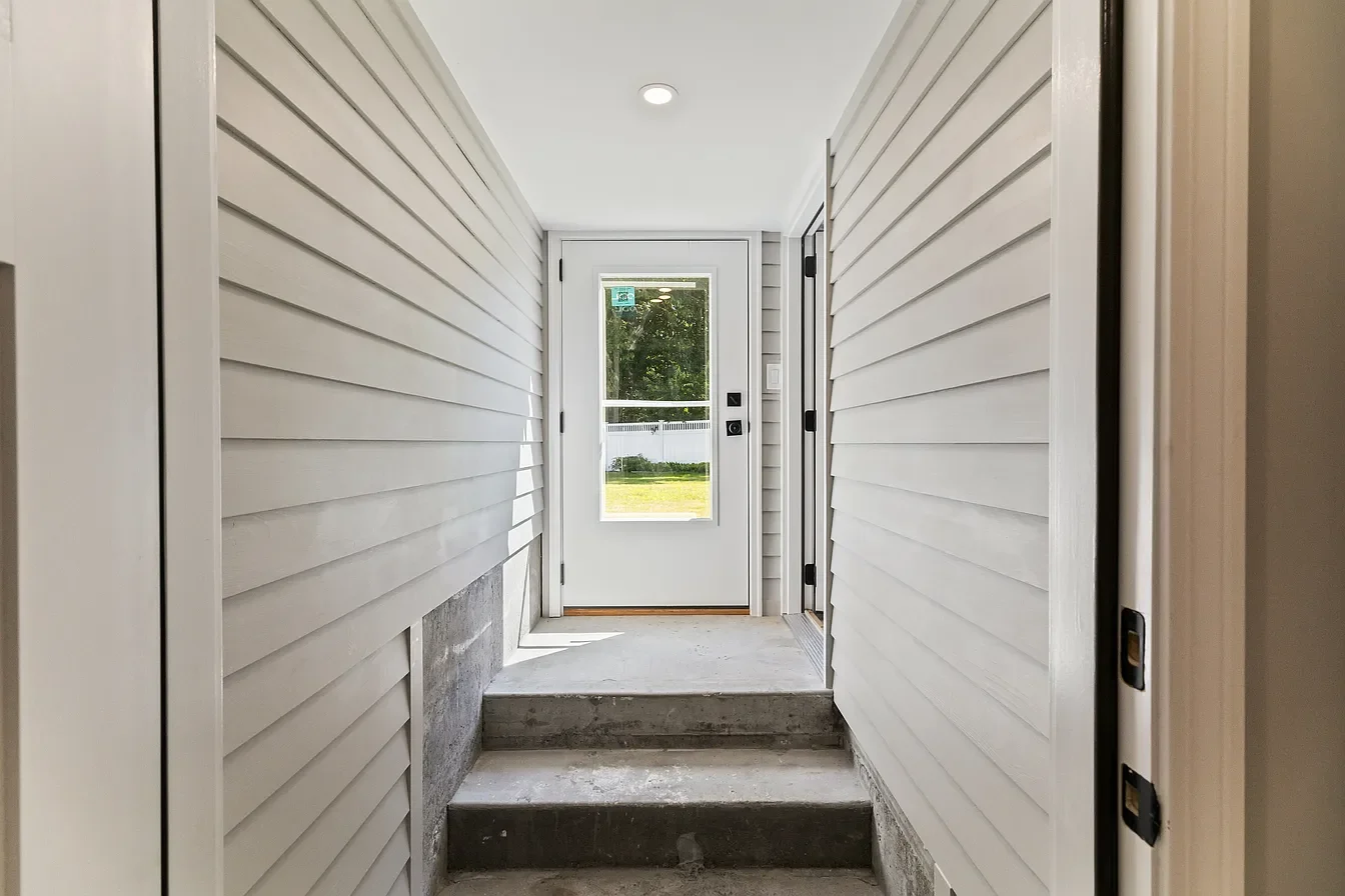 View of a home entrance with steps leading up to a glass door, white siding walls, and a small green yard visible outside.