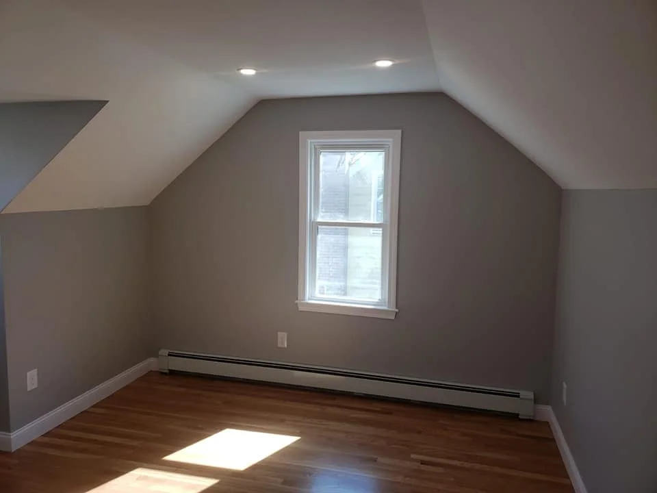 Empty room with gray walls, hardwood floors, a single window, and ceiling lights.