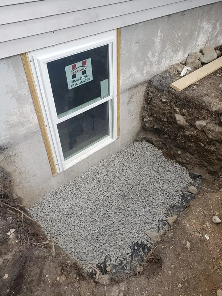 Construction site with a small window on the house and gravel poured on the ground outside.