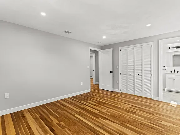 Empty room with hardwood floors, white walls, recessed lighting, a door opening, and a closet with white louvered doors.