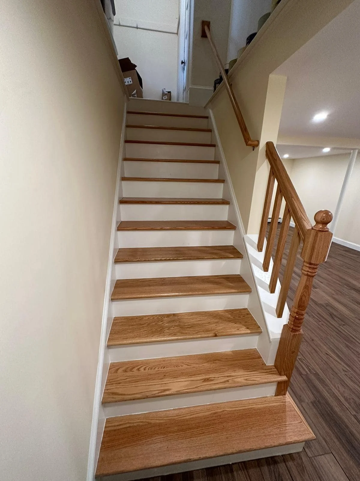 Wooden staircase with natural wood steps and white risers, featuring a wooden handrail on the right side, leading to an upper level in a home interior.