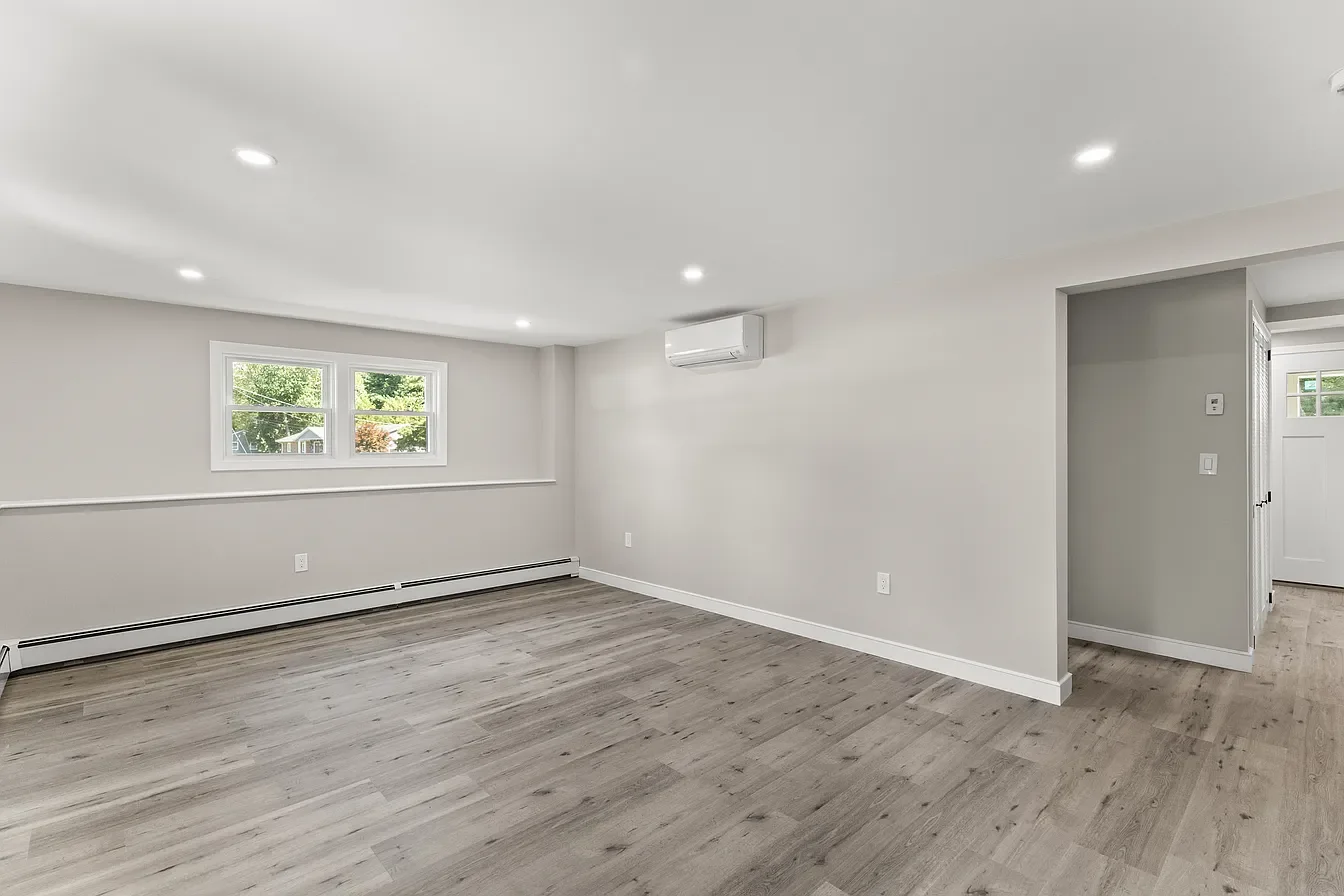 Empty living room with white walls, wood flooring, a window, and an air conditioning unit.