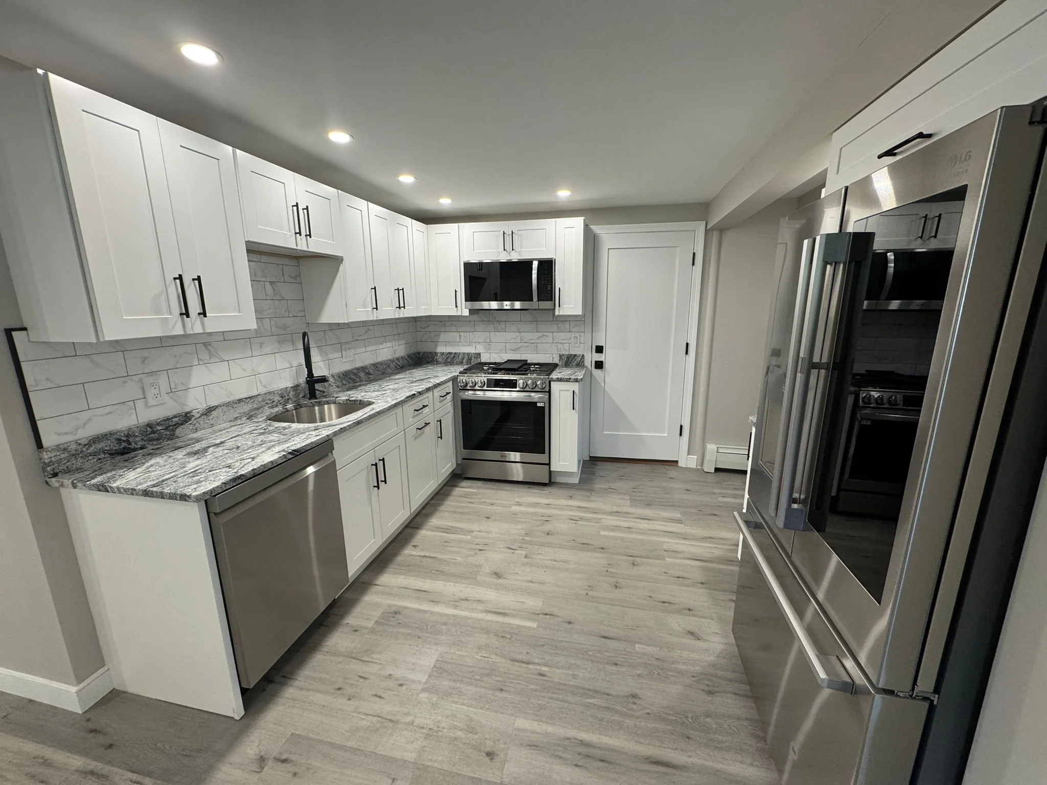 Modern kitchen with white cabinets, marble backsplash, granite countertops, stainless steel appliances, and light wood flooring.