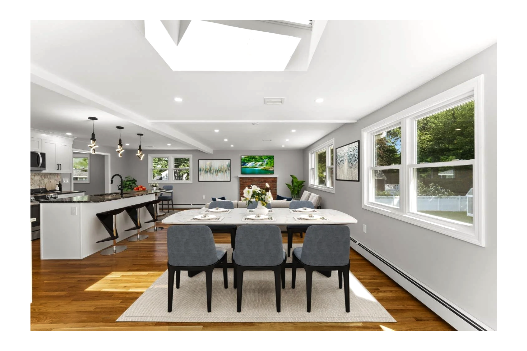 Bright open-concept kitchen and dining area with hardwood floors, large windows, and modern decor, including a kitchen island with black bar stools, a dining table with gray chairs, and artwork on the walls.