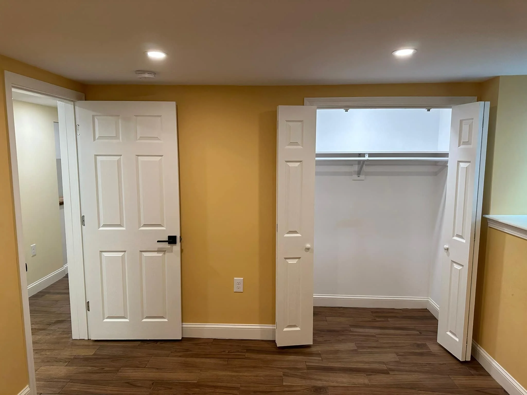 Interior of a room with a yellow wall, open closet with white doors and clear shelving, and a door on the left side.