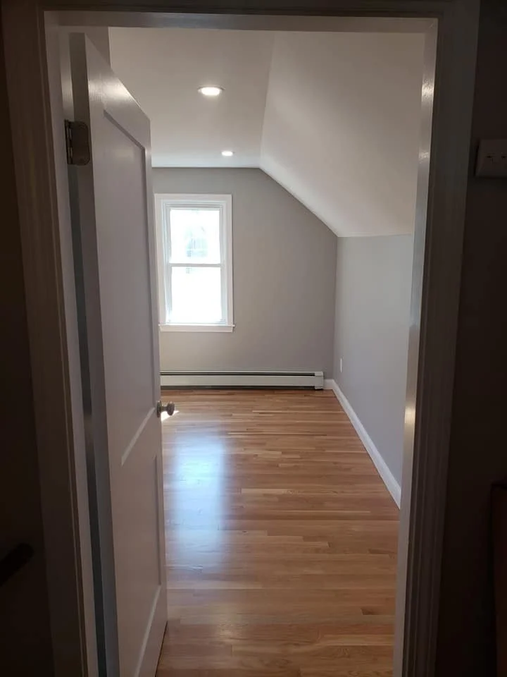 Empty room with hardwood floors, a window, and a sloped ceiling.