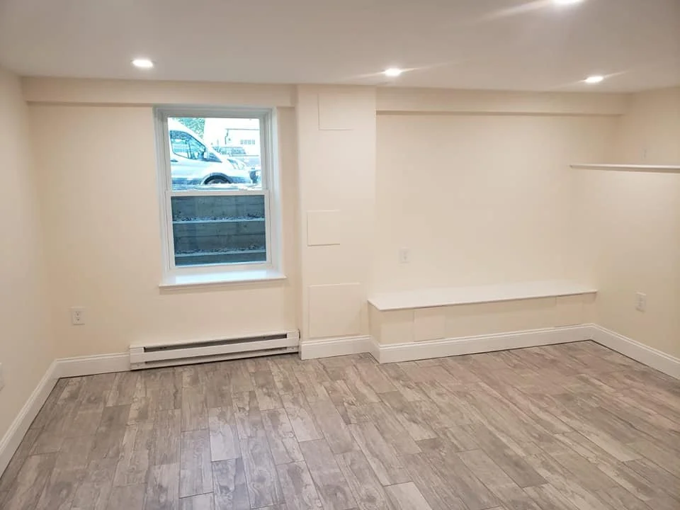 Empty room with a window, beige walls, wood flooring, and built-in bench.