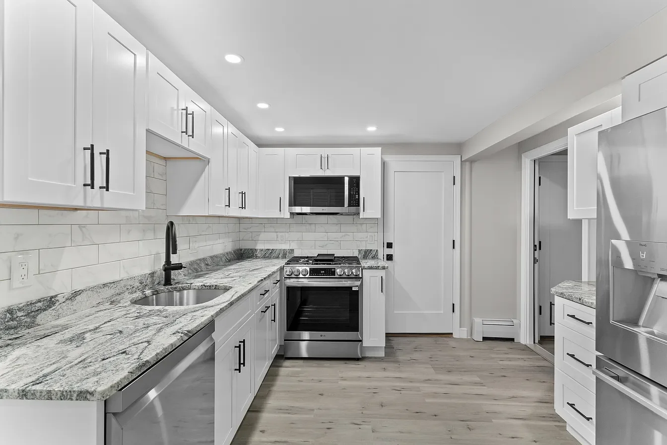 Modern kitchen with white cabinetry, granite countertops, stainless steel appliances, and hardwood floors.