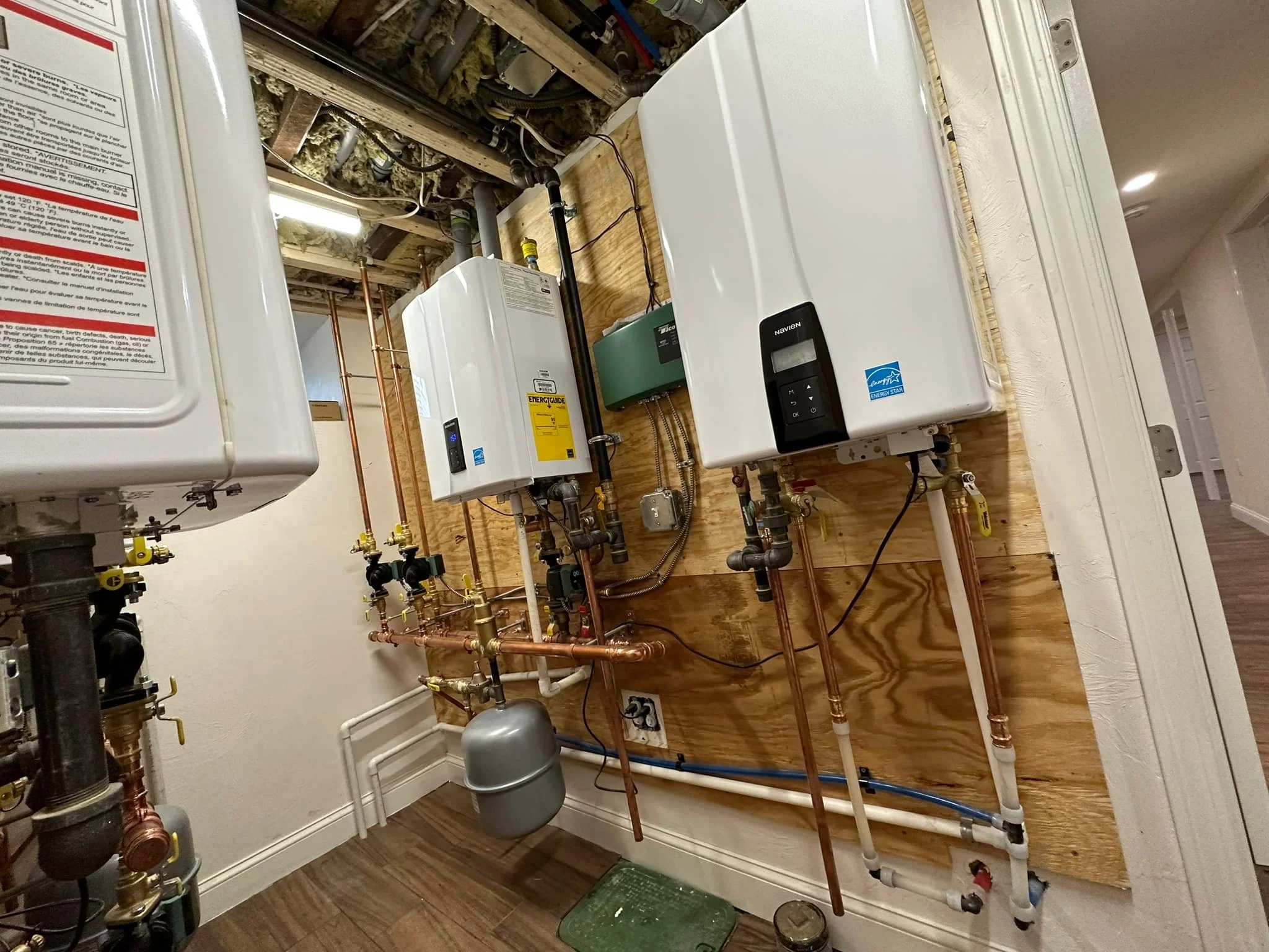 A utility closet with a wooden back wall housing water heater, water softener, and plumbing pipes.